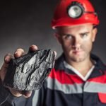 Coal miner showing lump of coal against a dark background